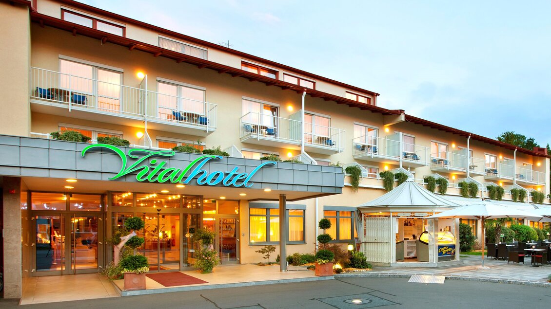 Ein einladendes Hotel mit modernen Balkonzimmern und einem stilvollen Eingangsbereich. Die Fassade ist freundlich gestaltet und es gibt eine Terrasse für Gäste. | © Vitalhotel der Parktherme