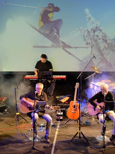 Eine Live-Band spielt auf der Bühne mit mehreren Musikern und Instrumenten. Im Hintergrund ist eine Leinwand mit einer Skisport-Darbietung zu sehen. | © Radkersburg 3