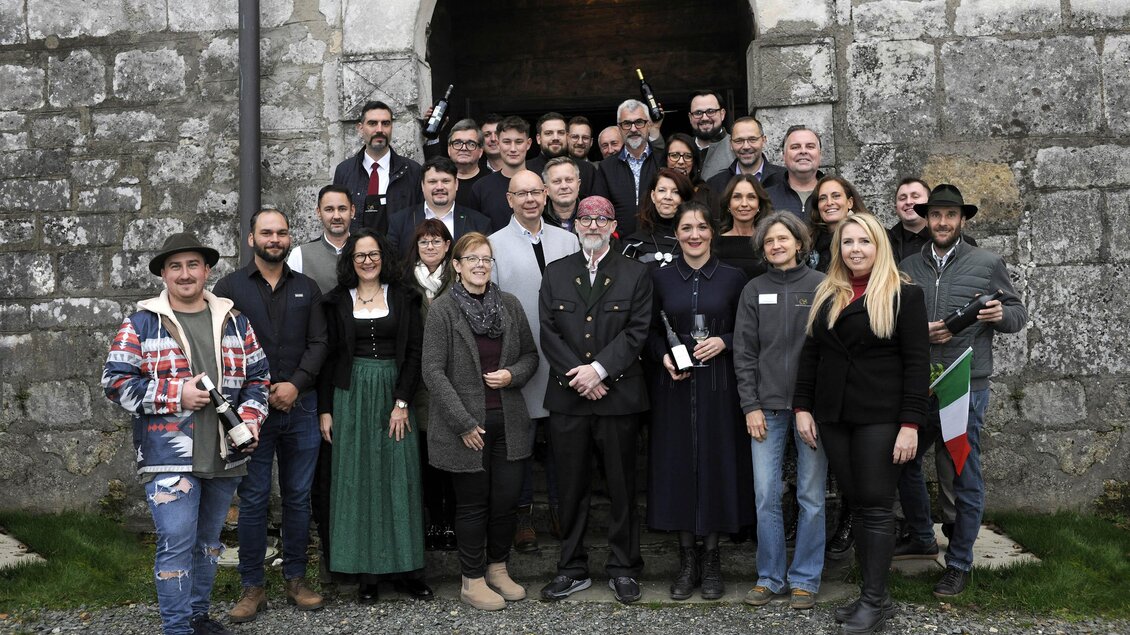 Eine Gruppe von Menschen steht vor einem historischen Eingang. Sie lächeln und posieren für das Foto. | © Apresvino