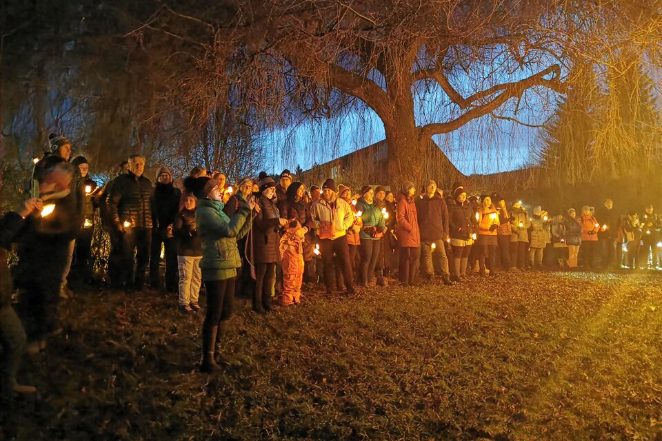 Eine Gruppe von Menschen steht im Freien bei Dämmerung und hält Kerzen in der Hand. Im Hintergrund ist ein großer Baum zu sehen. | © CDM