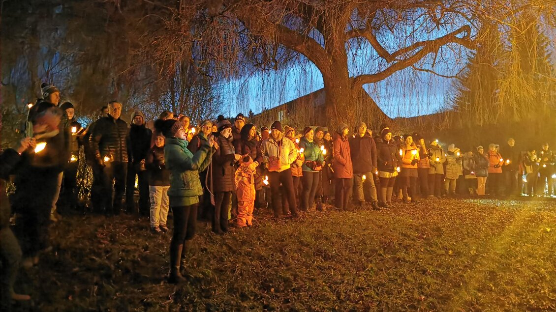 Eine Gruppe von Menschen steht im Freien bei Dämmerung und hält Kerzen in der Hand. Im Hintergrund ist ein großer Baum zu sehen. | © CDM
