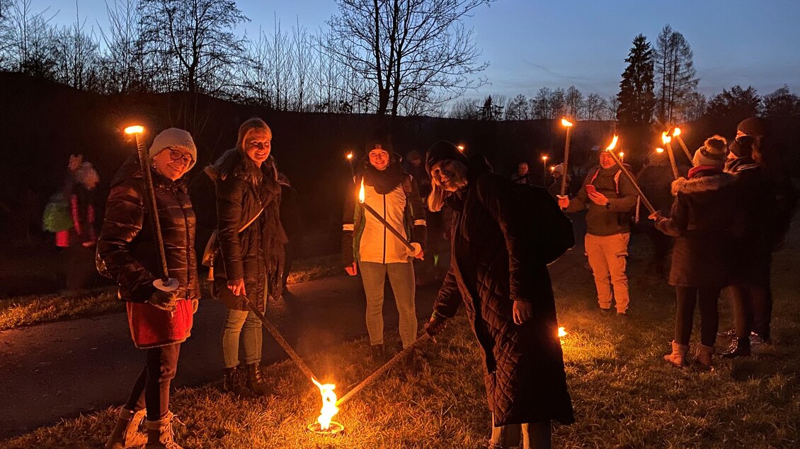Eine Gruppe von Menschen steht in der Dämmerung und hält Fackeln. Einige von ihnen zünden ihre Fackeln an, während die Umgebung ruhig und dunkel ist. | © CDM