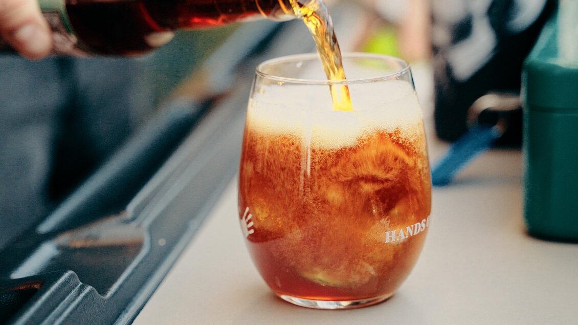 Ein Glas wird mit einem Getränk gefüllt, das schaumig aussieht. Im Hintergrund sind verschwommen Gegenstände zu sehen. | © Dietmar Kump
