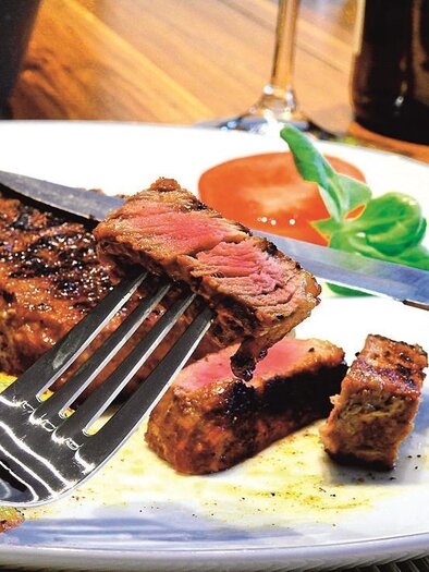 Ein saftiges Steak auf einem Teller mit Beilagen wie Kartoffeln und einem Salatblatt. Der Tisch ist mit Holz und einem Glas Wein dekoriert. | © BK Weiz  und ARGE Bergbauern Weiz