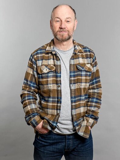 Ein Mann steht lächelnd vor einem grauen Hintergrund. Er trägt ein karierter Hemd und Jeans. | © ©Andrea Sojka