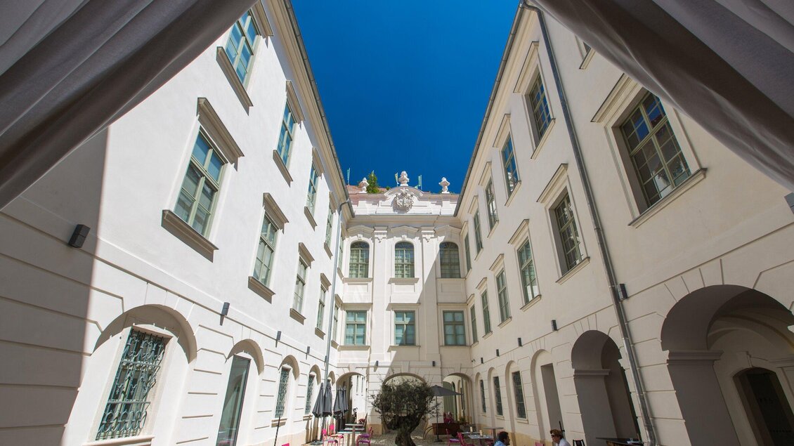 Ein heller Innenhof zwischen weißen Gebäuden. Der blaue Himmel ist gut sichtbar und es gibt eine gemütliche Atmosphäre. | © Graz Tourismus - Harry Schiffer