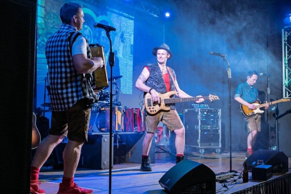 Eine Band spielt auf einer Bühne mit bunten Lichtern und Rauch. Die Musiker tragen fesche Kleidung und spielen verschiedene Instrumente. | © Günter Simmerl
