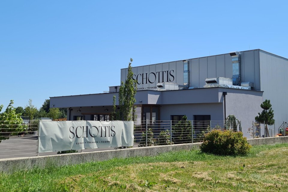 Ein modernes Gebäude mit der Aufschrift "Schottis" in einer grünen Umgebung. Die Sonne scheint klar am blauen Himmel. | © Christine Schwetz