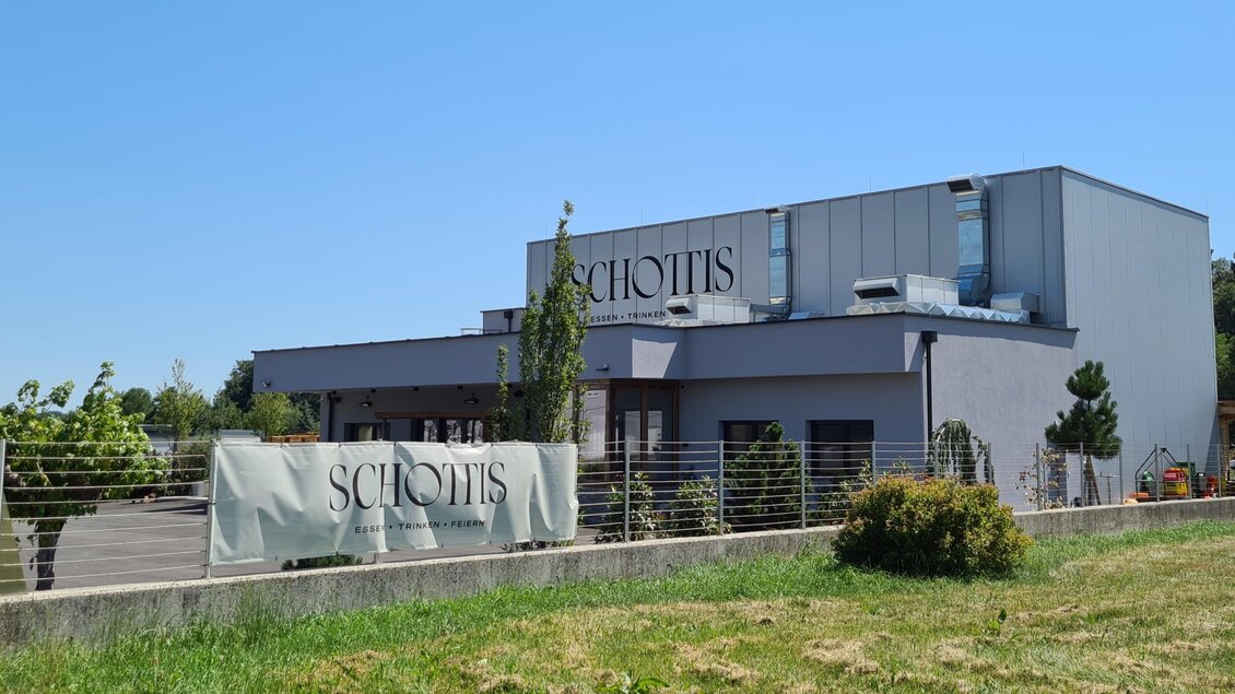 Ein modernes Gebäude mit der Aufschrift "Schottis" in einer grünen Umgebung. Die Sonne scheint klar am blauen Himmel. | © Christine Schwetz