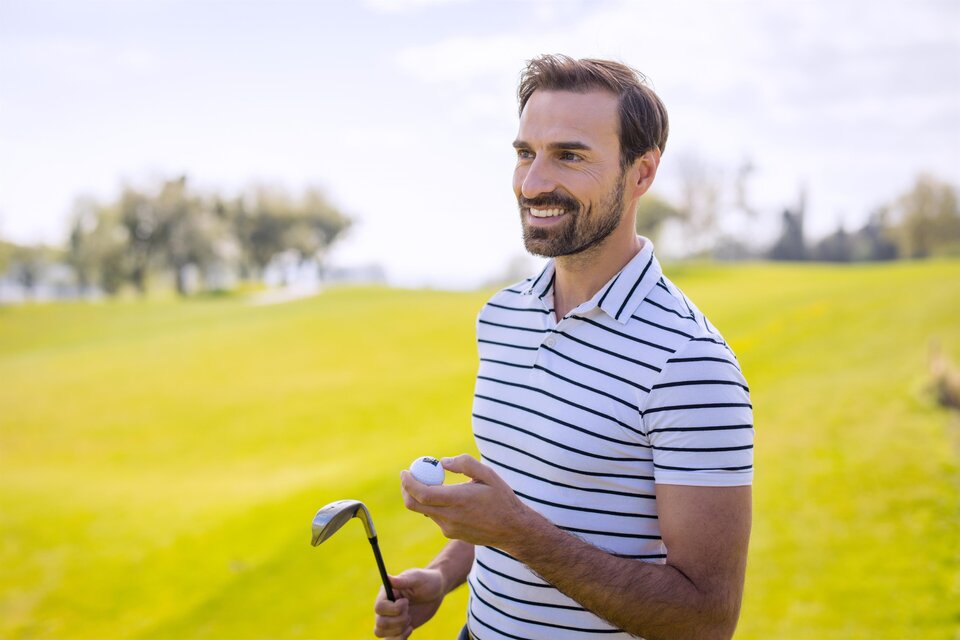 Ein lächelnder Mann steht auf einem Golfplatz und hält einen Golfschläger sowie einen Golfball in der Hand. Im Hintergrund ist saftig grünes Gras zu sehen. | © TV BW