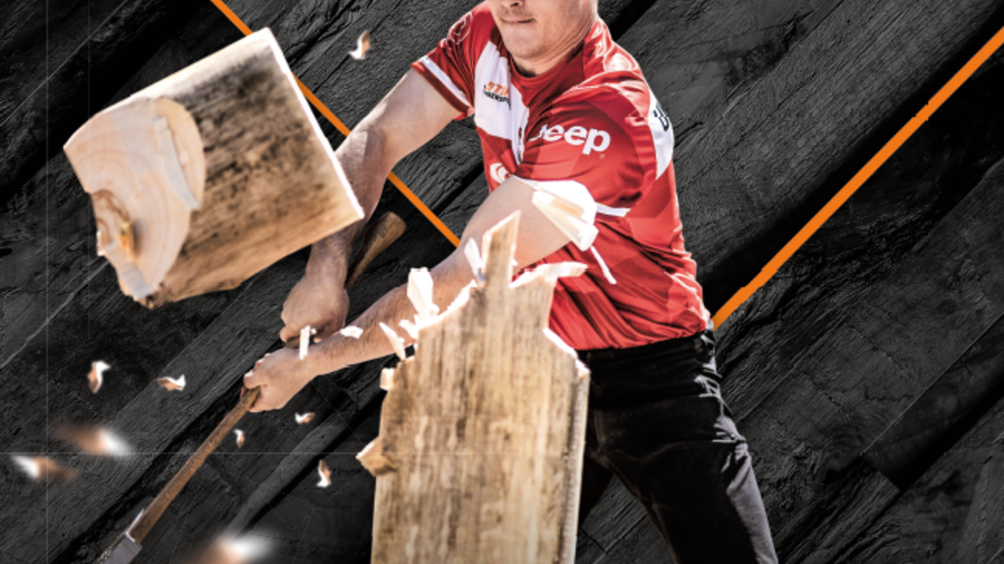Ein Athlet, der mit einer Axt auf einen Baumstamm zielt, während Holzspäne fliegen. Im Hintergrund sind Sponsorenlogos und Informationen zu einem Timbersport-Event in Schladming. | © Stihl