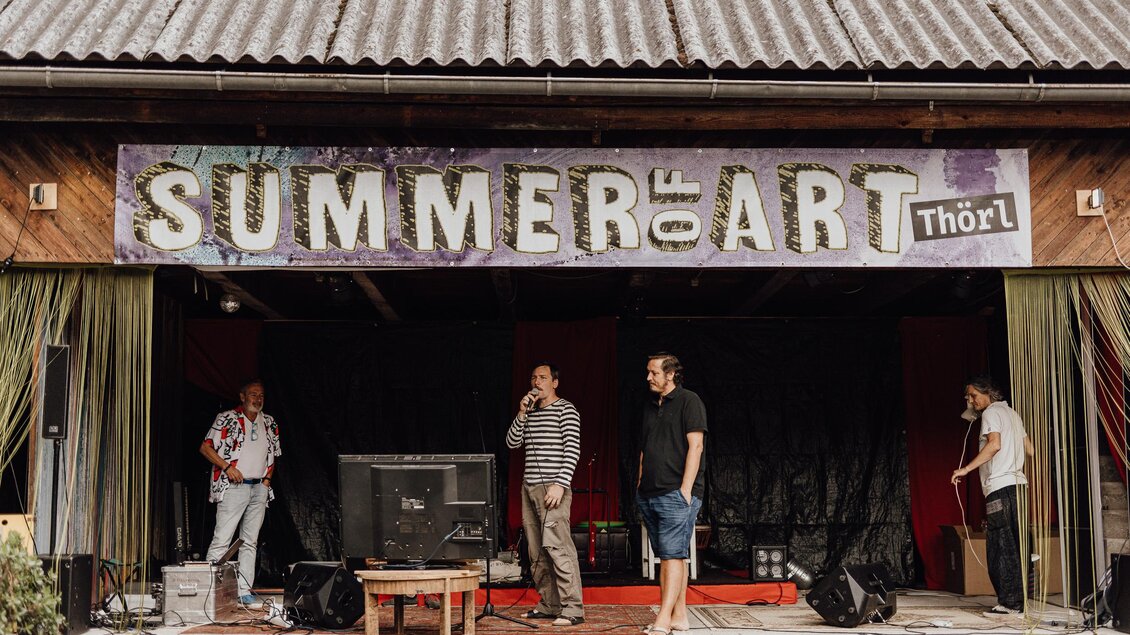 Eine Bühne mit einem Banner für "SUMMER of ART" in Thörl. Vier Männer stehen vor dem Aufbau, bereit für die Veranstaltung. | © nicoleseiser.at