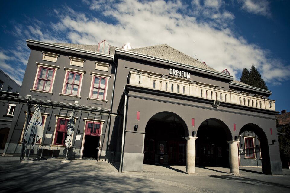 Ein historisches Gebäude mit dem Namen "Orpheum". Es hat eine elegante Fassade und einen klaren, blauen Himmel im Hintergrund. | © Spielstätten - Lupi Spuma