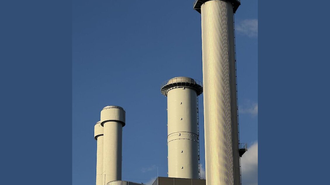 Drei hohe, zylindrische Schornsteine einer Industrieanlage mit Metallverkleidung und Wartungsplattformen vor blauem Himmel. | © Sascha Paar