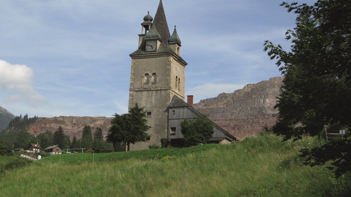 Ein historisches Gebäude mit dekorativen Fassadenmalereien und Fenstern. Im Hintergrund sind Berge zu sehen, bei klarem Himmel. | © Hermann Buder