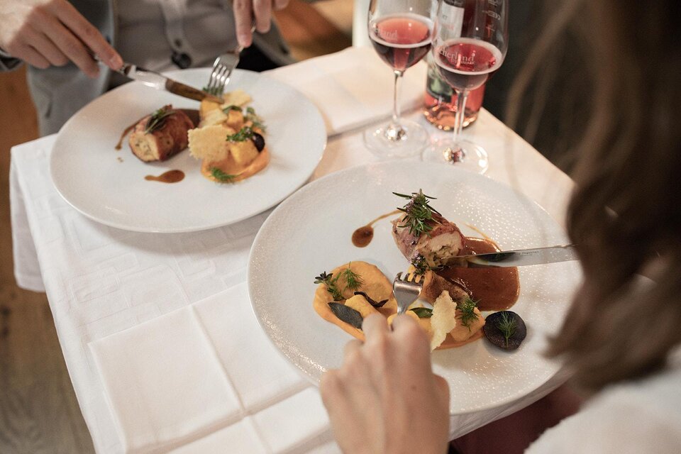 Zwei Personen genießen ein elegantes Essen in einem Restaurant. Auf den Tellern befinden sich kunstvoll angerichtete Gerichte und Gläser mit Roséwein. | © TV Südsteiermark - achromaticphotography
