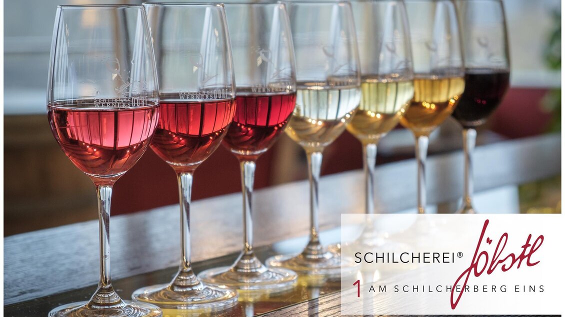 Eine Auswahl an Weingläsern mit verschiedenen Weinsorten in bunten Farben. Im Hintergrund ist das Logo eines Weingeschäfts zu sehen. | © Florian Jöbstl