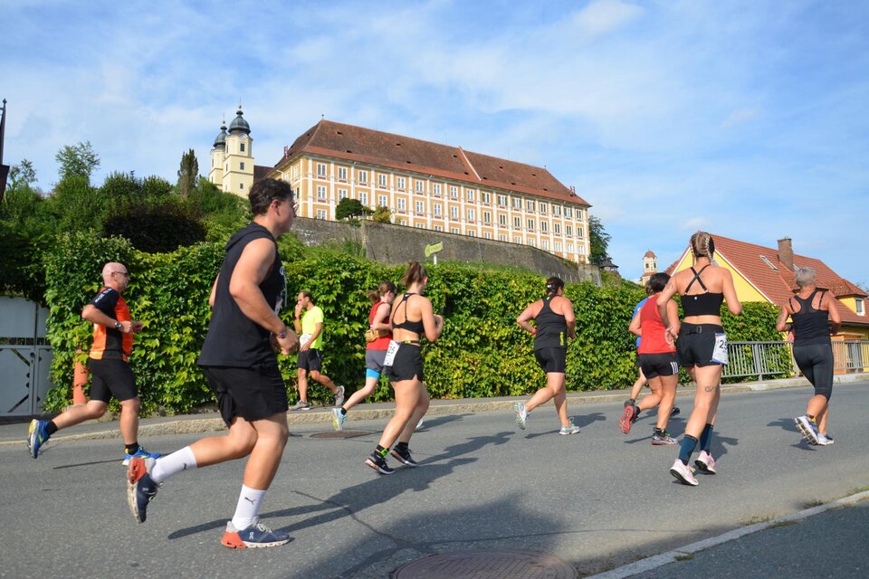 Eine Gruppe von Läufern joggt auf einer Straße. Im Hintergrund ist ein historisches Gebäude unter einem blauen Himmel zu sehen. | © TV Südsteiermark - Gölles FC Sauzipf