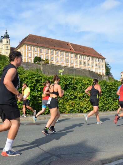 Eine Gruppe von Läufern joggt auf einer Straße. Im Hintergrund ist ein historisches Gebäude unter einem blauen Himmel zu sehen. | © TV Südsteiermark - Gölles FC Sauzipf