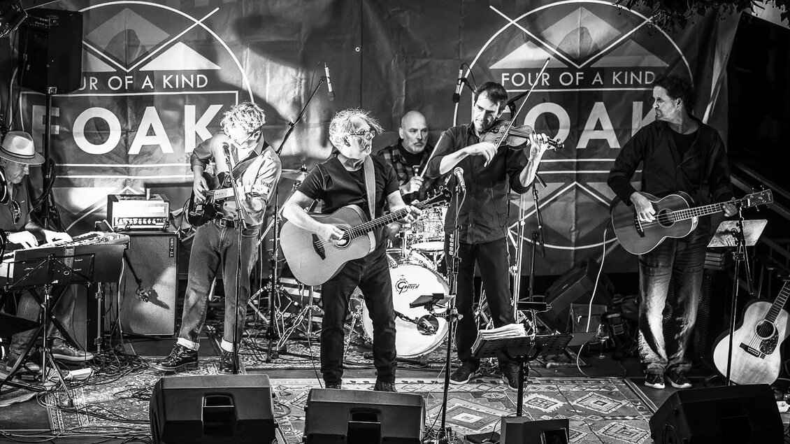 Eine lebhafte Band mit mehreren Musikern spielt auf einer Bühne. Es gibt Gitarre, Geige und Keyboards, während die Musiker in einer dynamischen Atmosphäre auftreten. | © FOAK