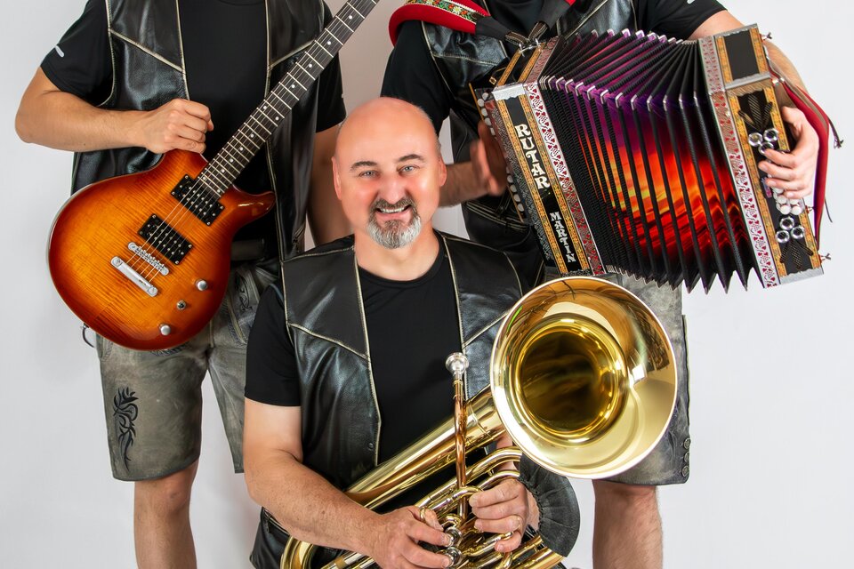 Drei Musiker posieren zusammen, einer hält eine Gitarre, der andere ein Akkordeon und der dritte ein Tuba. Alle tragen ähnlicheoutfits und lächeln freundlich in die Kamera. | © Silberklang