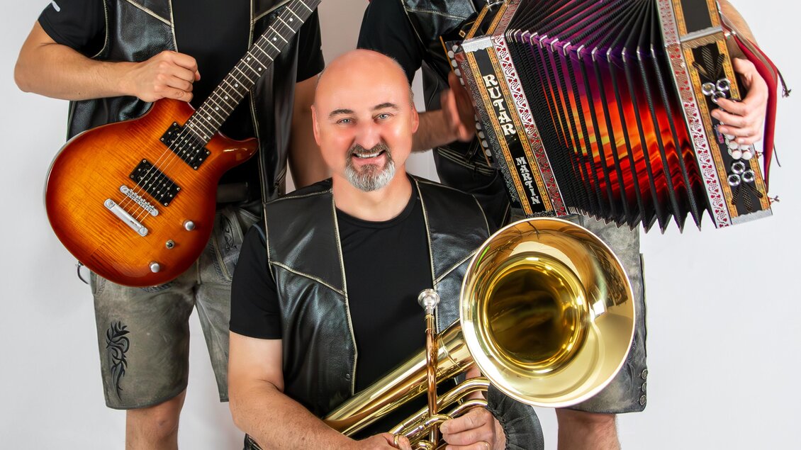 Drei Musiker posieren zusammen, einer hält eine Gitarre, der andere ein Akkordeon und der dritte ein Tuba. Alle tragen ähnlicheoutfits und lächeln freundlich in die Kamera. | © Silberklang