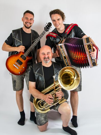 Drei Musiker posieren zusammen, einer hält eine Gitarre, der andere ein Akkordeon und der dritte ein Tuba. Alle tragen ähnlicheoutfits und lächeln freundlich in die Kamera. | © Silberklang