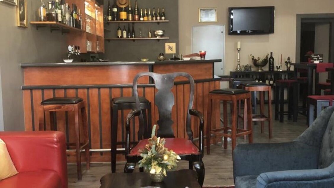 Eine gemütliche Lounge mit einem roten Sofa, einem schicken Tisch und Barhockern. Im Hintergrund befindet sich eine gut ausgestattete Bar und ein Fernseher. | © Christian Bernhard