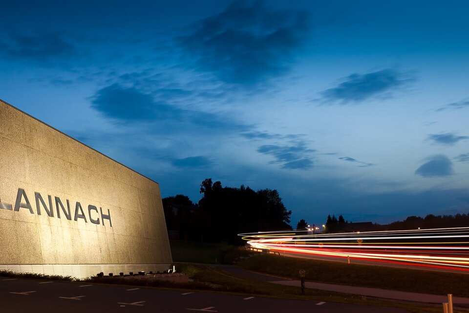 Ein modernes Gebäude mit dem Schriftzug "LANNACH" bei Dämmerung. Die Umgebung ist ruhig und es sind einige Lichtspuren von Fahrzeugen zu sehen. | © MG Lannach - Petru Rimovetz