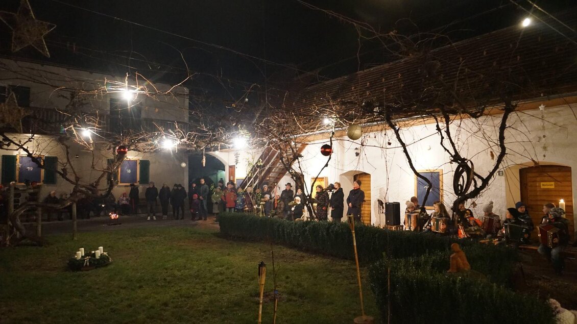 Ein stimmungsvoller Innenhof mit festlicher Beleuchtung in der Abenddämmerung. Menschen versammeln sich an verschiedenen Stellen und genießen die Atmosphäre.