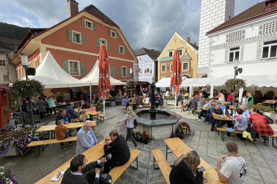 Ein belebter Marktplatz mit vielen Tischen und Menschen. Bunte Gebäude und Zelte schaffen eine gemütliche Atmosphäre. | © Thomas Rauninger