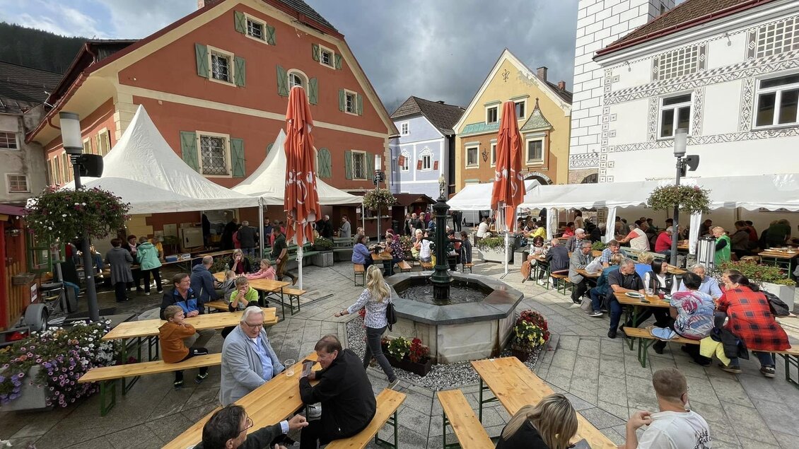 Ein belebter Marktplatz mit vielen Tischen und Menschen. Bunte Gebäude und Zelte schaffen eine gemütliche Atmosphäre. | © Thomas Rauninger