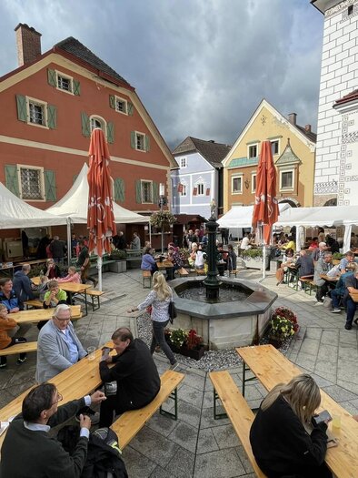 A bustling marketplace with many tables and people. Colorful buildings and tents create a cozy atmosphere. | © Thomas Rauninger