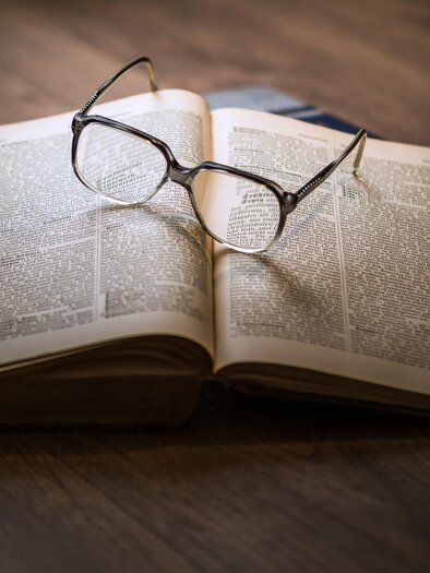 Ein aufgeschlagenes Buch liegt auf einem Tisch. Eine Brille ruht auf den Seiten des Buches. | © Pixabay