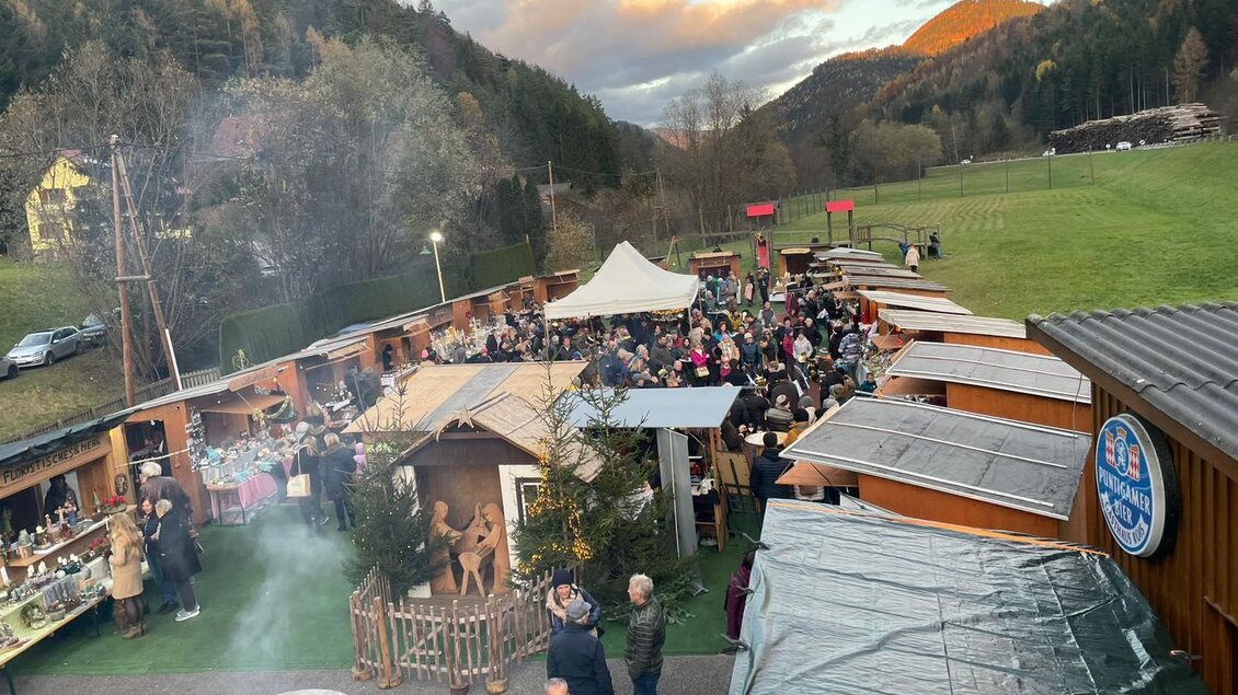 Ein belebter Weihnachtsmarkt mit vielen Ständen und Besuchern. Im Hintergrund sind Hügel und Bäume zu sehen, die eine festliche Atmosphäre schaffen. | © Stadtgemeinde Frohnleiten