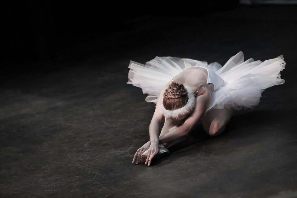 Eine Ballettänzerin in einem weißen Tutu vollführt eine elegante Pose auf der Bühne. Ihr Gesichtsausdruck zeigt Konzentration und Anmut. | © Pixabay