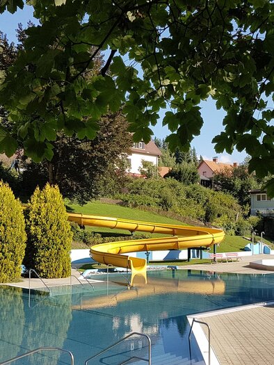 A swimming pool with various slides and clear water. In the background, green trees and a building can be seen. | © Stadtgemeinde Judenburg