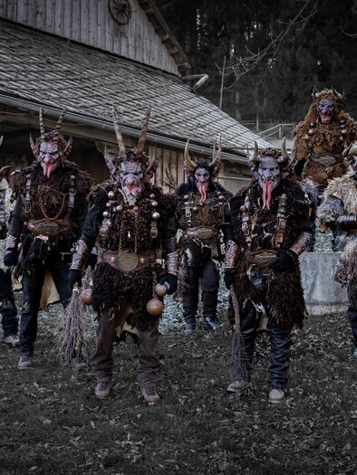 Eine Gruppe von verkleideten Personen mit Hörnern und auffälligen Kostümen steht vor einem Holzhaus. Die Umgebung wirkt mystisch und geheimnisvoll. | © Marktgemeinde Kraubath