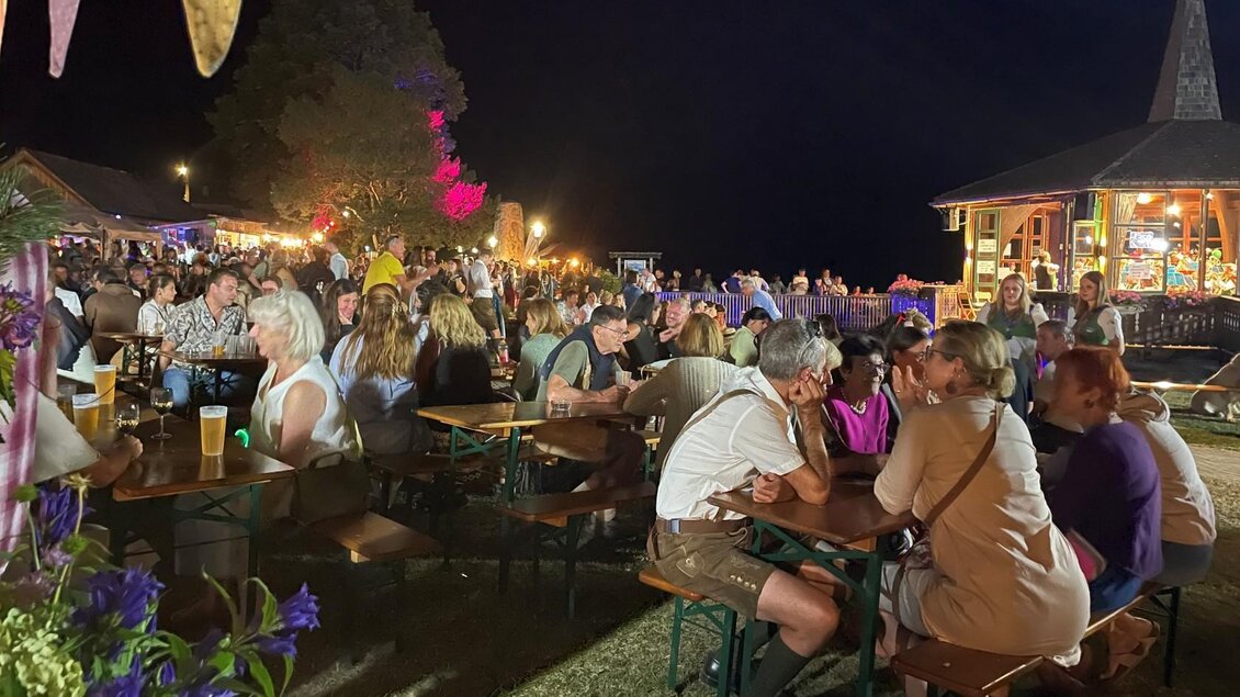 Eine lebhafte Festveranstaltung bei Nacht mit vielen Menschen an Tischen. Bunte Lichter und Stände sorgen für eine fröhliche Atmosphäre. | © Bettina Scheck
