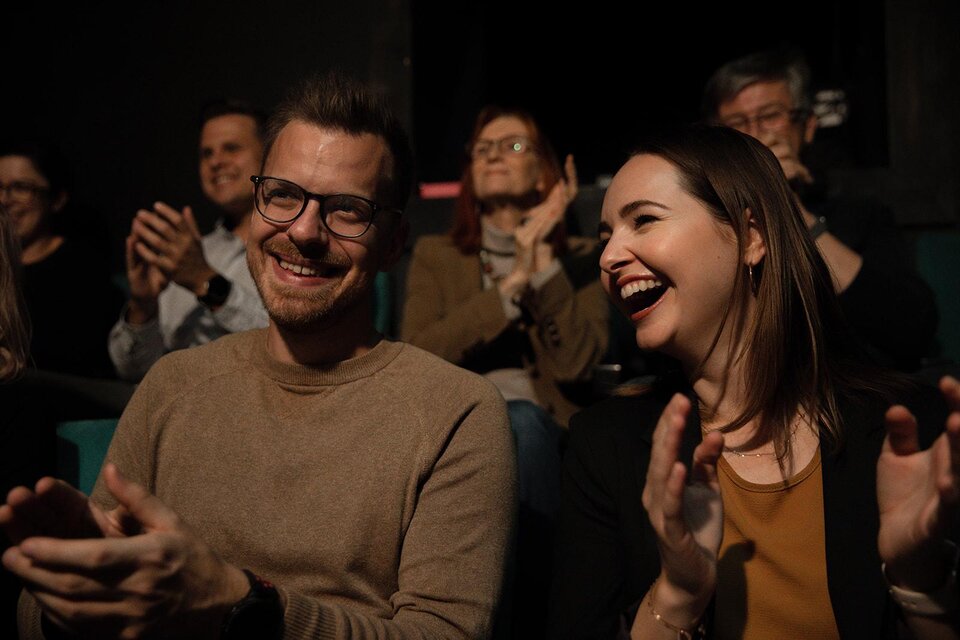Ein fröhliches Paar sitzt im Publikum und applaudiert. Beide lachen und genießen die Atmosphäre der Veranstaltung. | © achromaticphotography