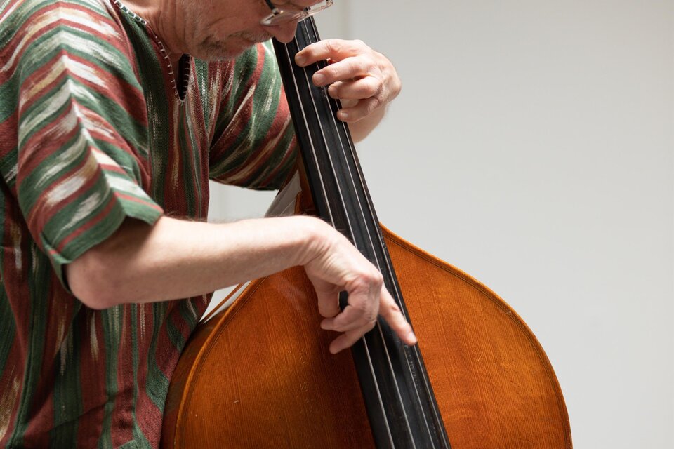 Ein Musiker spielt Kontrabass. Er trägt ein gestreiftes Hemd und konzentriert sich auf sein Spiel. | © TVB Südsteiermark – Achromatic Photography