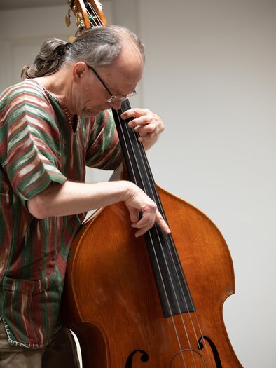 A musician is playing double bass. He is wearing a striped shirt and is focused on his playing. | © TVB Südsteiermark – Achromatic Photography