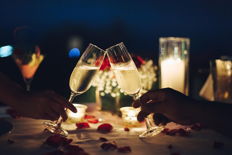 Ein romantisches Dinner bei Nacht mit Sektgläsern, die angestoßen werden. Der Tisch ist mit Blütenblättern und Kerzen dekoriert. | © TV Südsteiermark