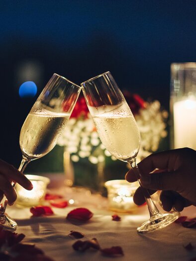 A romantic dinner at night with champagne glasses being clinked. The table is decorated with flower petals and candles. | © TV Südsteiermark