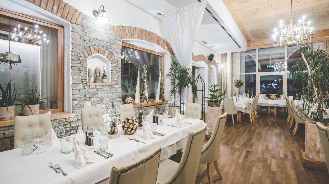 Ein elegantes Restaurant mit großen Fenstern und stilvoller Einrichtung. Die Tische sind festlich gedeckt und es gibt viele Pflanzen. | © Garten Hotel Ochensberger