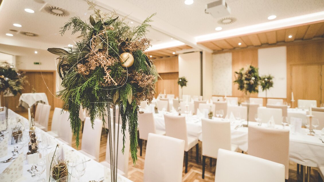 Ein eleganter Speisesaal mit festlich dekorierten Tischen. Große Blumenarrangements aus Pflanzen zieren die Tische und schaffen eine einladende Atmosphäre. | © Garten Hotel Ochensberger