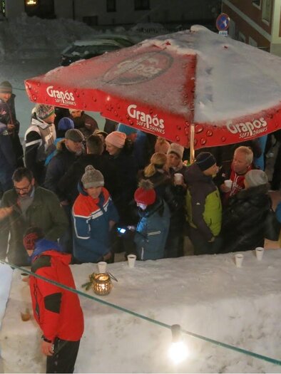 A large crowd gathers under a red sunshade in the snow. The scene takes place at night in a winter setting. | © Bergrettung