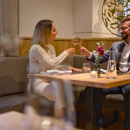 Ein elegantes Restaurant mit einem Tisch, an dem ein Paar anstößt. Die Atmosphäre ist gemütlich und einladend. | © MotionManager_Chris Zarfl