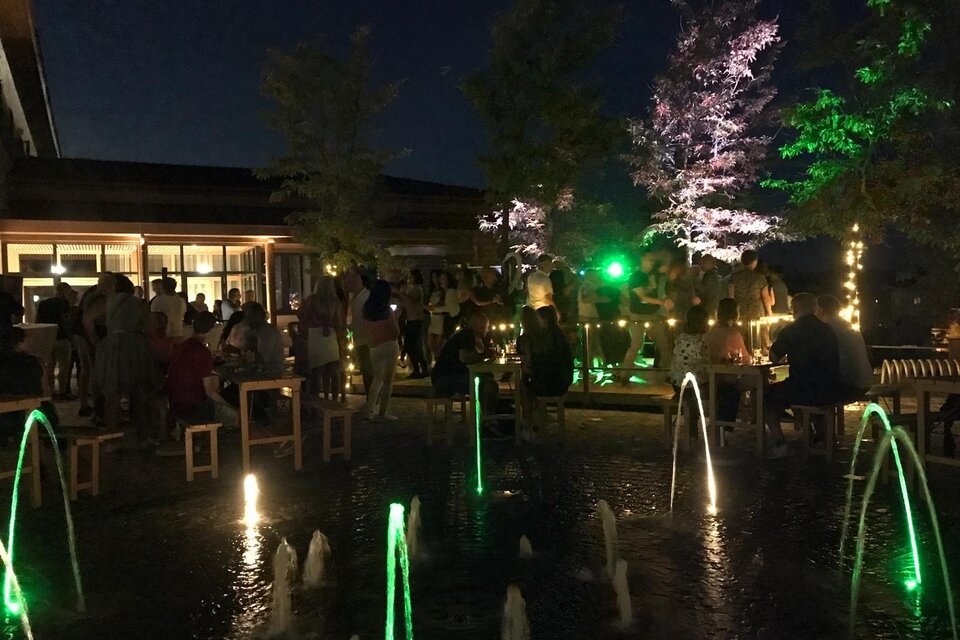 Eine lebhafte Nacht mit vielen Menschen und bunten Lichtern. Im Vordergrund sprudeln Wasserfontänen in einem kleinen Teich. | © Josef Zirkl