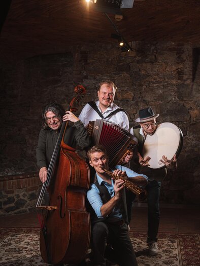 A group of four musicians poses in an old room. They play various instruments like double bass, accordion, and flute. | © reithofer_media